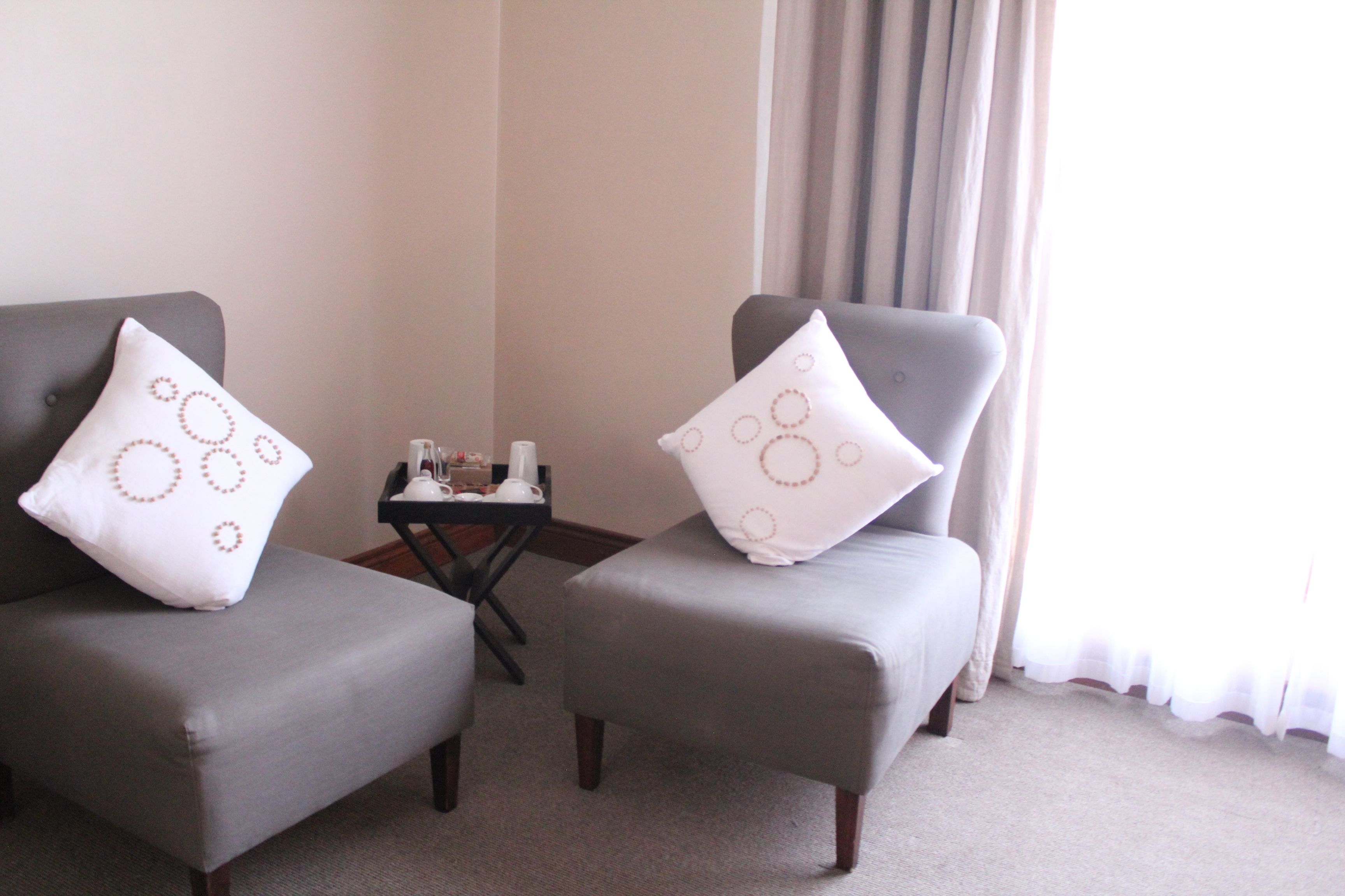 Two grey armchairs with matching white pillows, a small table with a lamp, and a window with curtains.