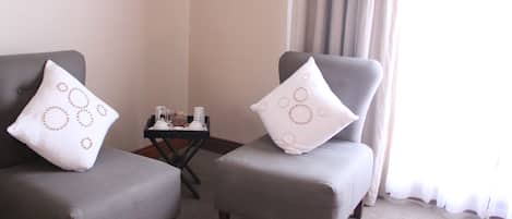 Two grey armchairs with matching white pillows, a small table with a lamp, and a window with curtains.