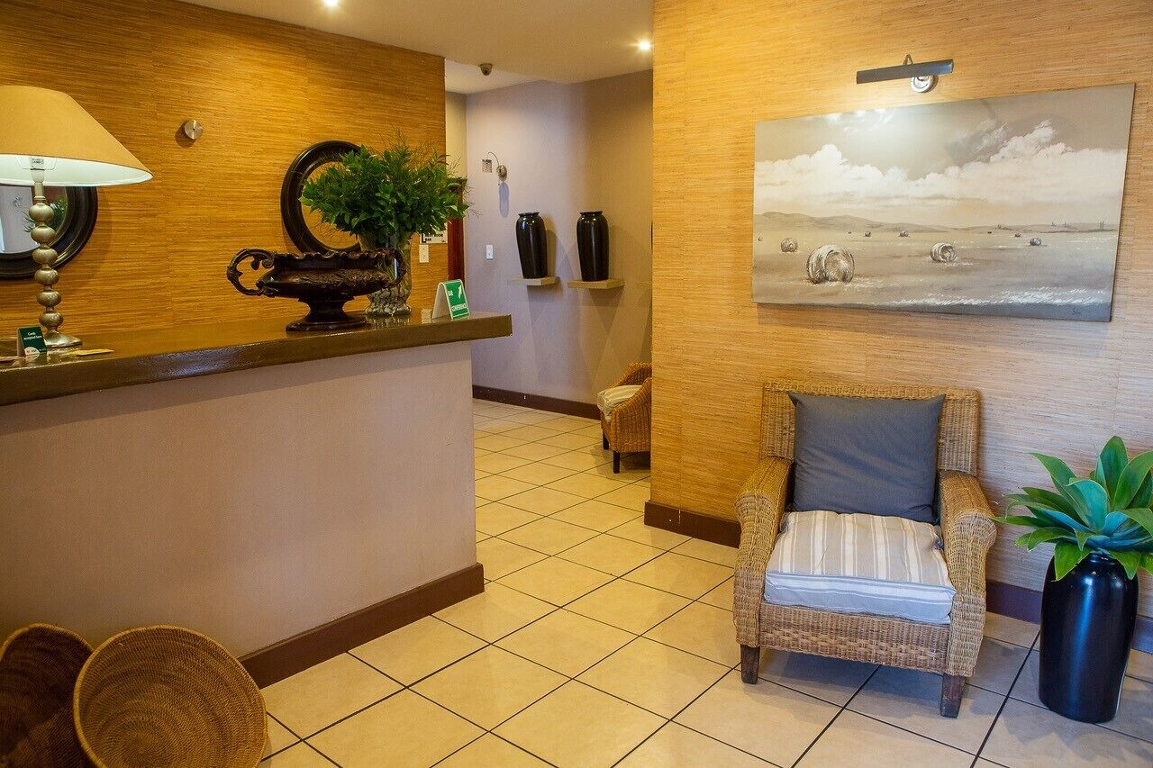 A reception area with a wooden reception desk, wicker chairs, a potted plant, and a wall-mounted painting.