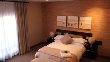 Habitación de hotel con una cama grande, dos mesitas de noche, cabecera y una obra de arte en la pared.