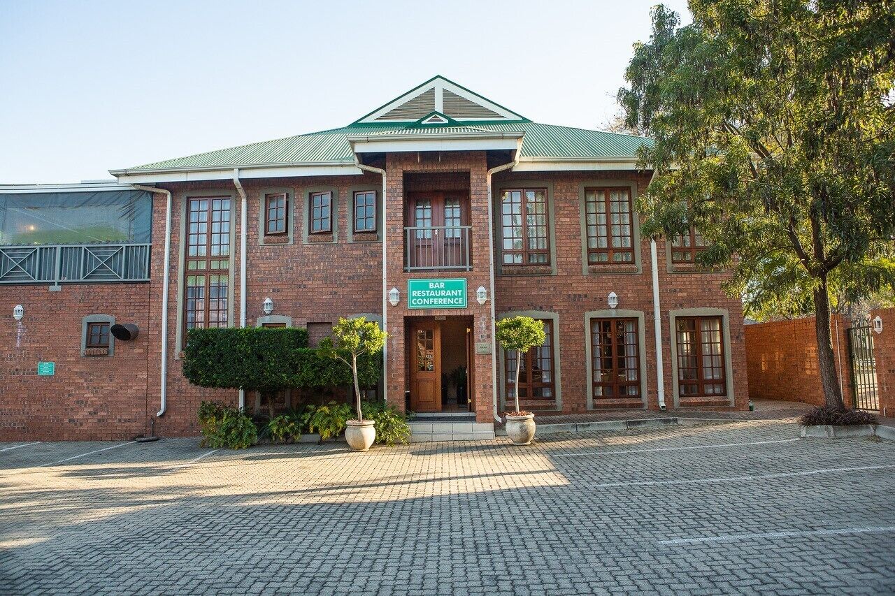A brick building with a green roof, a sign reading "BAR RESTAURANT CONFERENCE", and a paved entrance area with potted plants.