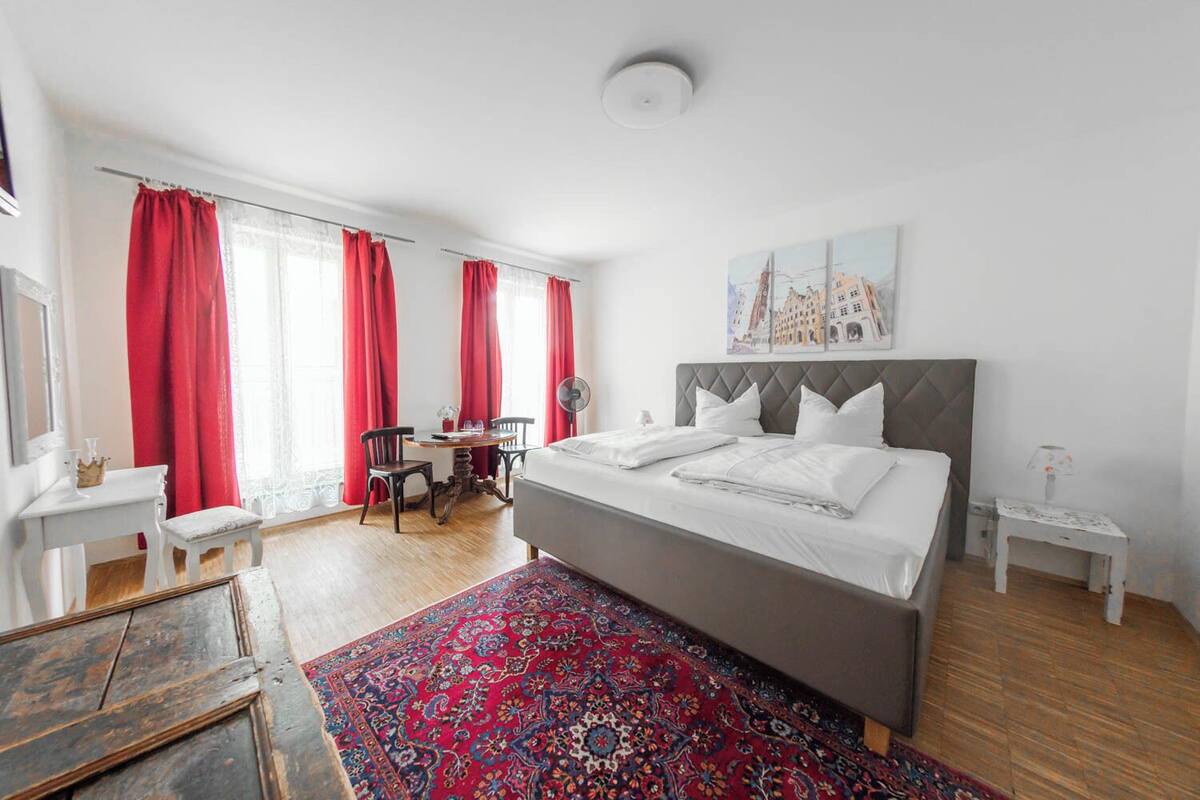 A bedroom with a large bed, a small table with chairs, and a red patterned rug.