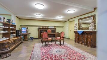 A spacious living room with a large red and white patterned rug, a wooden coffee table, two chairs, a television, and a decorative cabinet with a mirror.