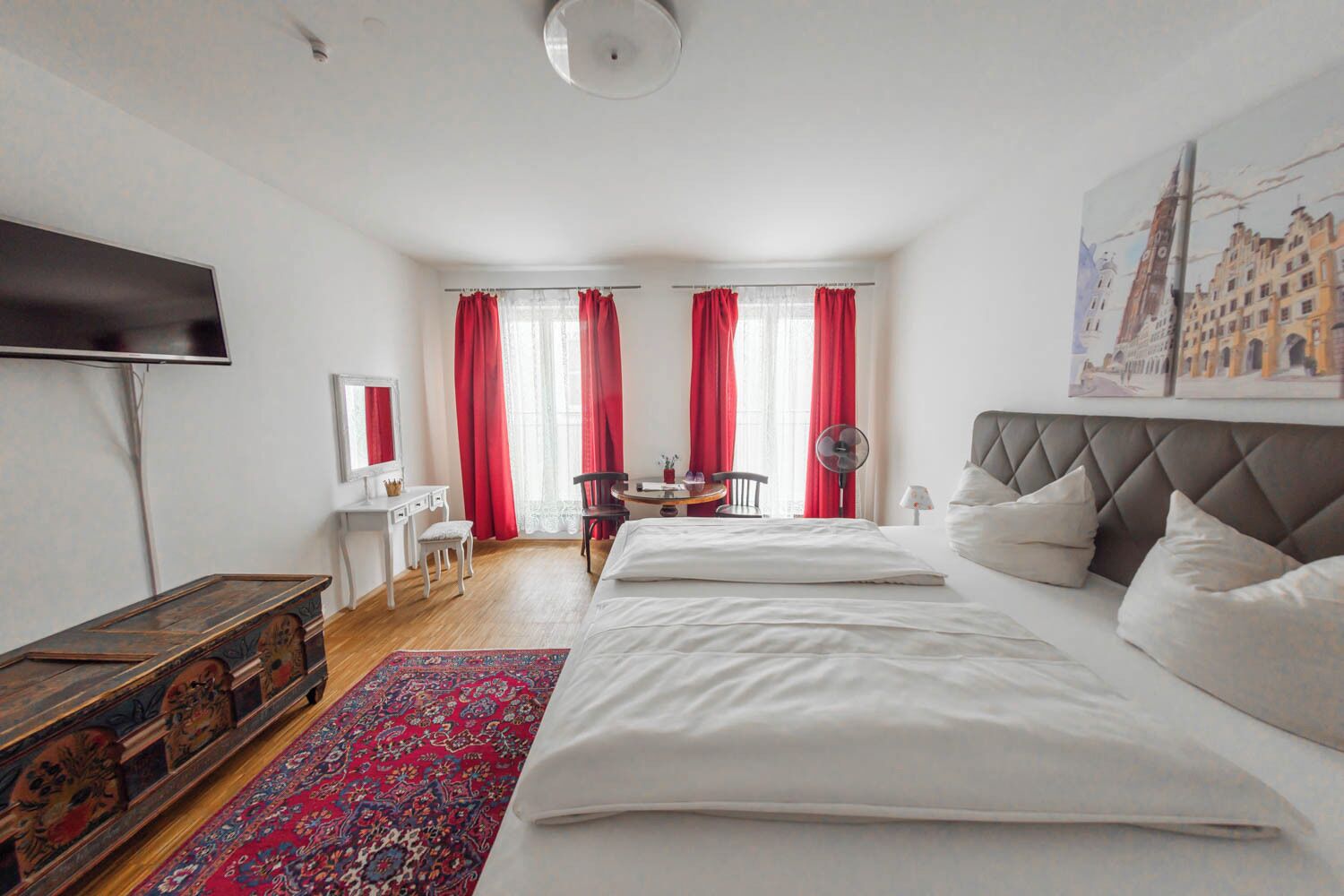A hotel room with a large bed, a desk with a chair, a TV, and a painting on the wall.