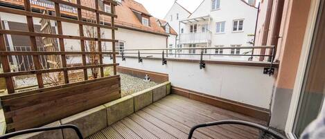 A balcony with wooden railings, a small garden area, and two wicker chairs.
