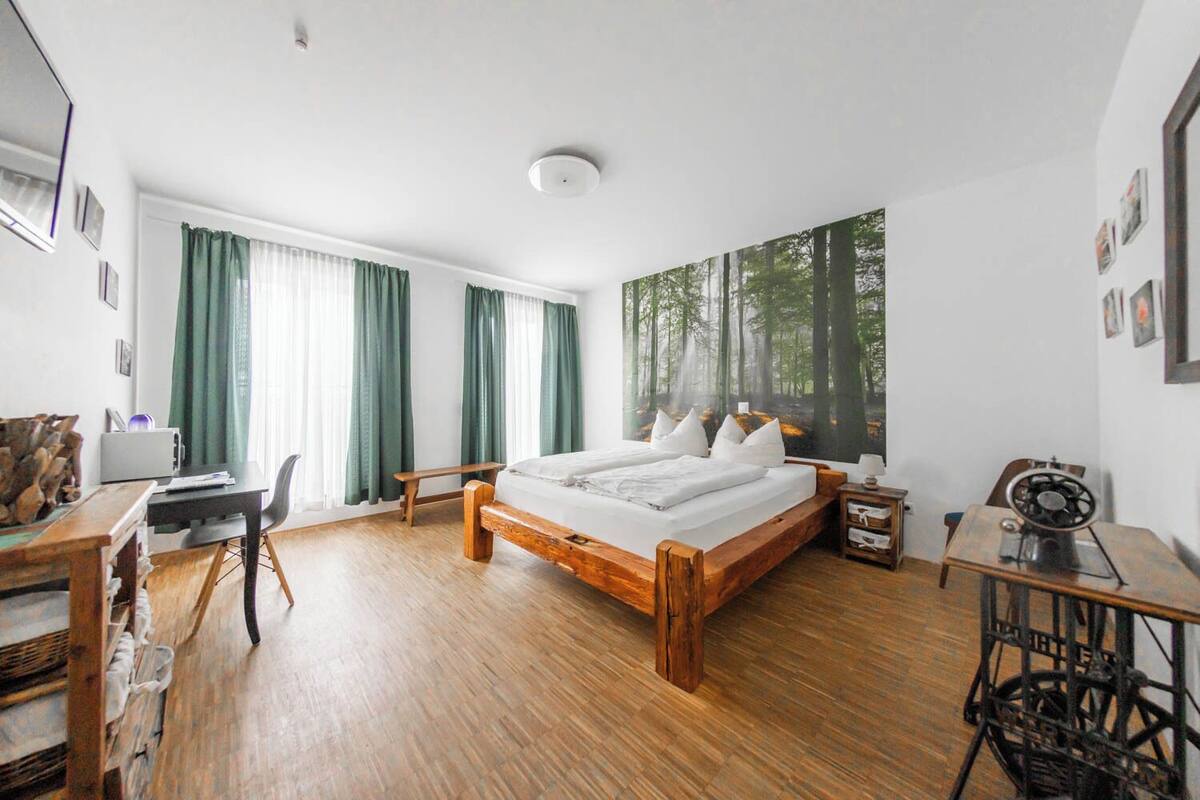 A bedroom with a wooden bed, a desk, a chair, and a large forest-themed wall mural.
