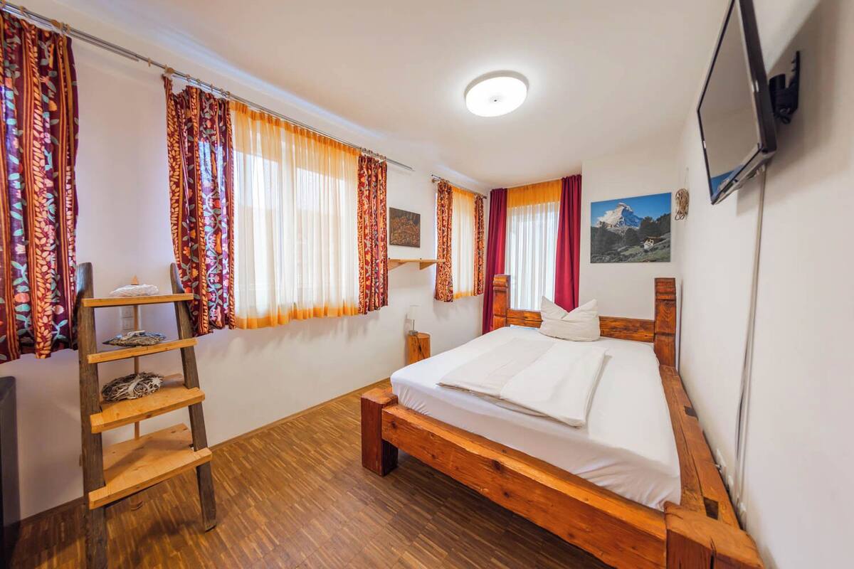A room with a wooden bed, a wooden shelf, and a TV mounted on the wall.