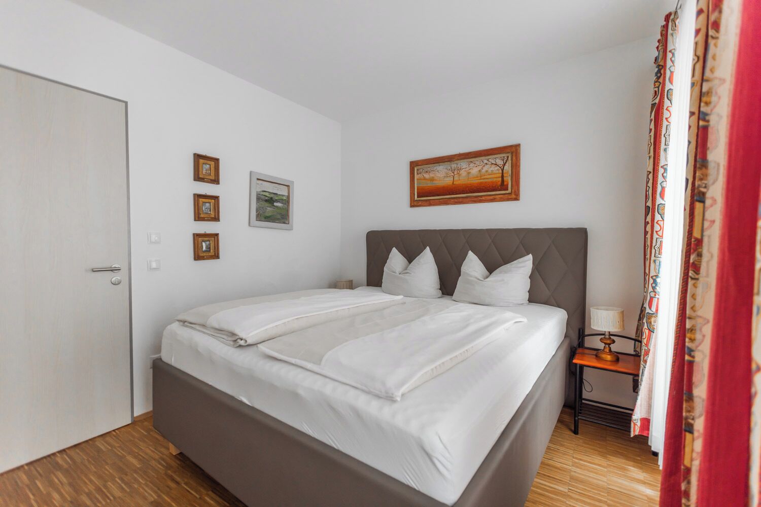 Una cama bien hecha con sábanas blancas, cabecera de madera y una mesita de noche con lámpara.