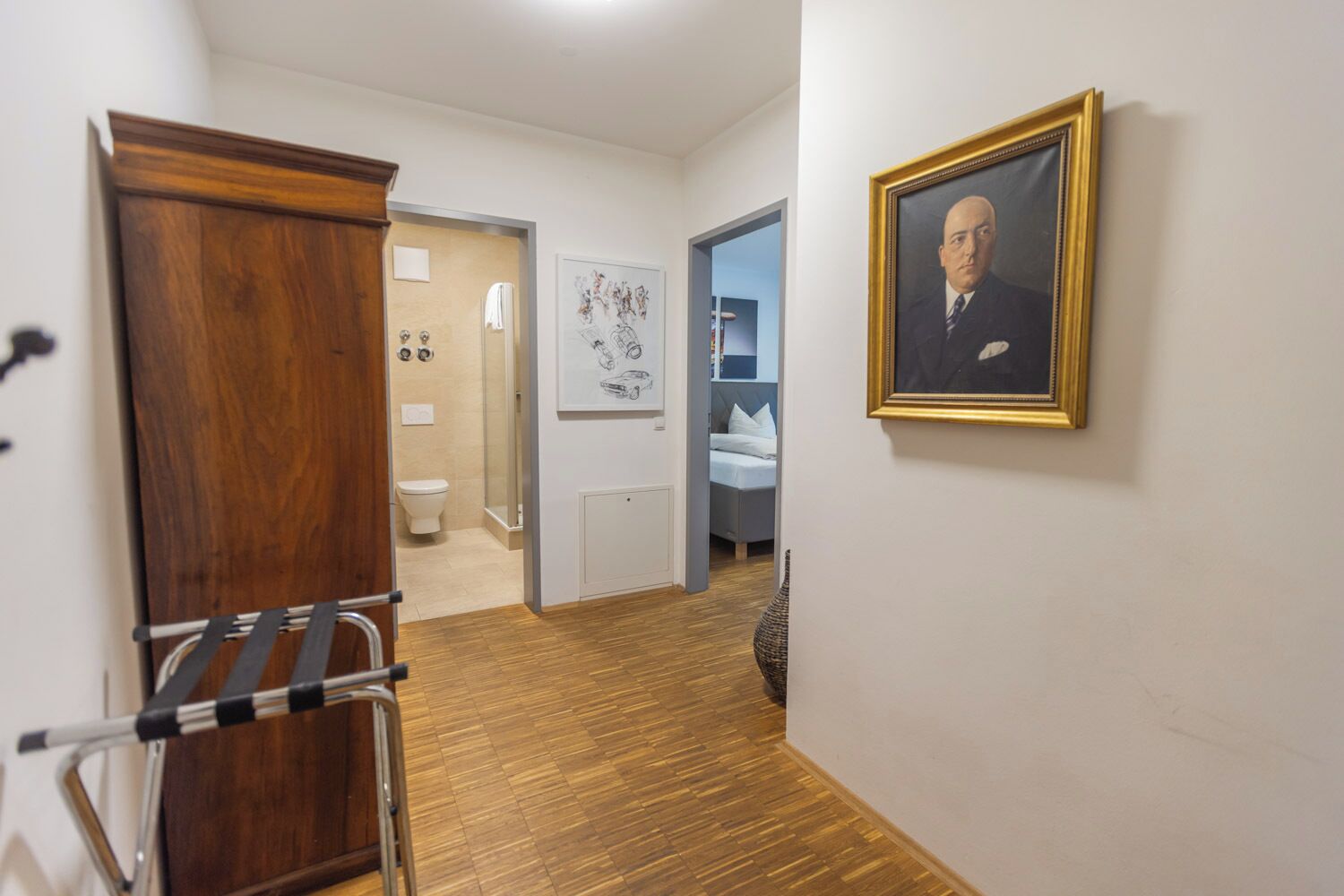 A hallway with a wooden wardrobe, a framed portrait on the wall, and a bathroom visible through an open door.