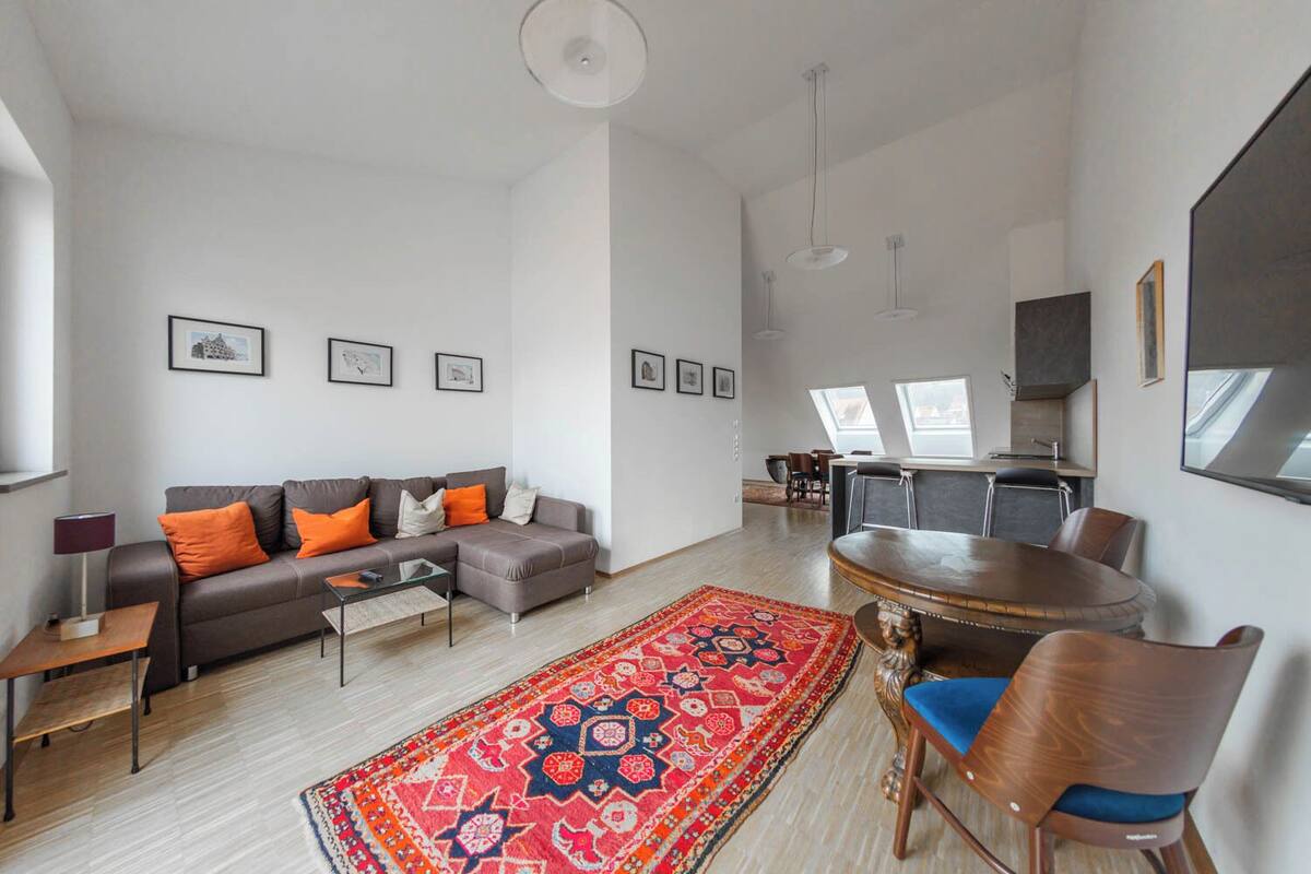 A modern living room with a sofa, coffee table, and a patterned rug. There is a dining area with a table and chairs.