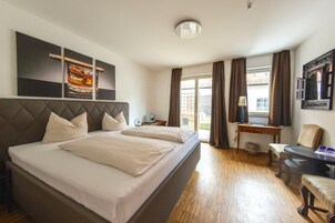 Habitación de hotel con una cama grande, un escritorio y una silla. Tiene una ventana con cortinas, una lámpara de techo y una obra de arte en la pared.