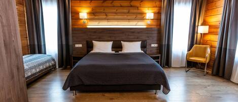 A wooden-paneled room with a large bed, a smaller bed, a chair, and two wall-mounted lamps.