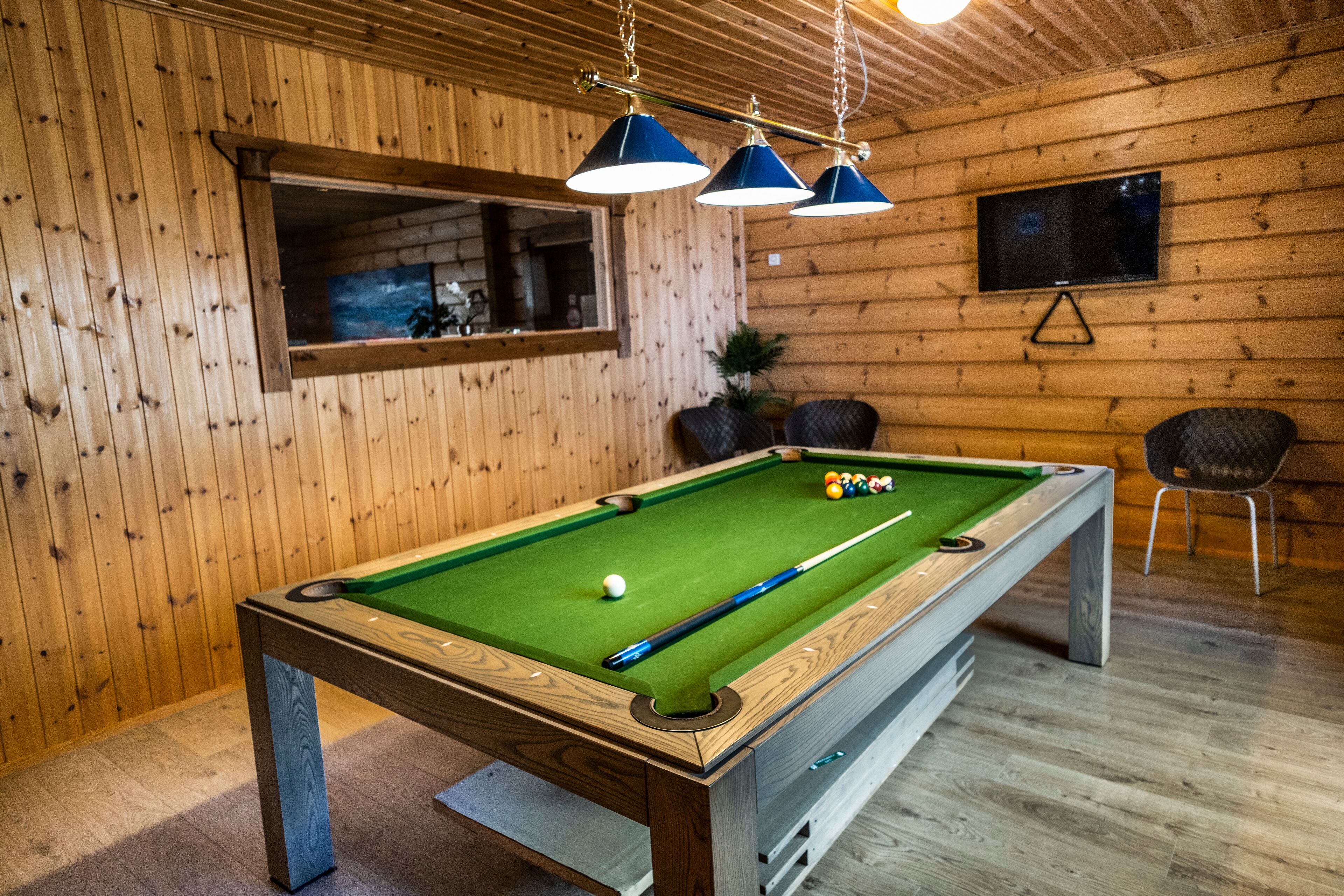 A pool table with balls, a television, and wooden walls.