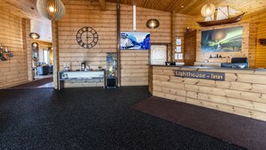 A wooden interior with a reception desk labeled "Lighthouse Inn," a clock, a television displaying a snowy mountain scene, and a ship model on the wall. - Lighthouse Inn (Suðurnesjabær)