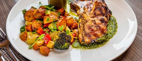 Un plato de comida con verduras asadas y carne, acompañado de una taza pequeña de salsa.