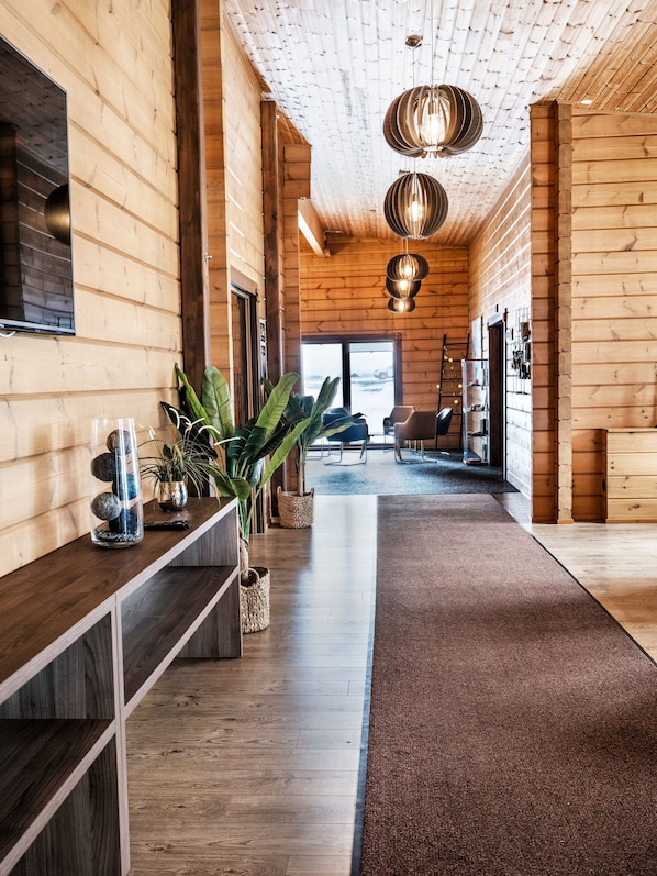 A wooden interior with a long hallway, a central plant, and a view to the outside. - Lighthouse Inn (Suðurnesjabær)