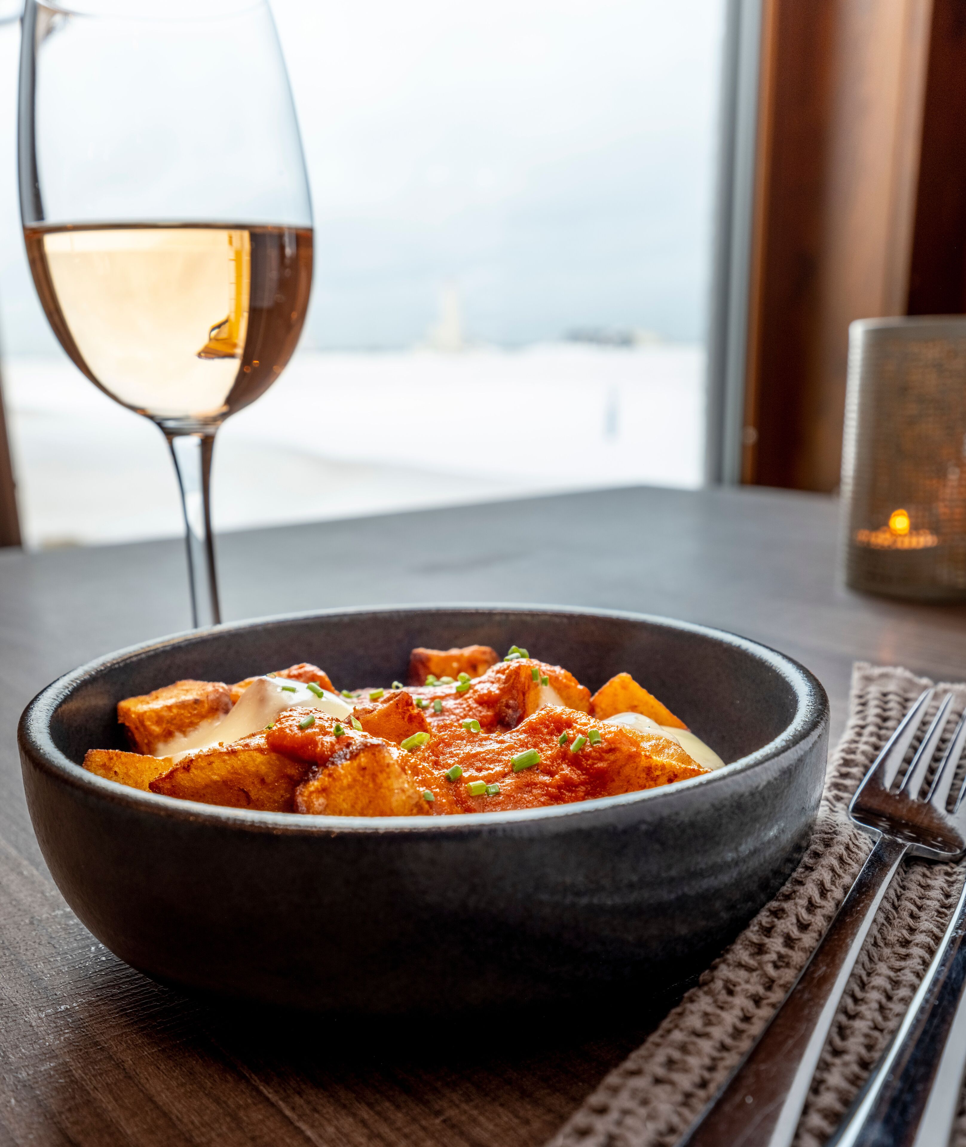 A bowl of food on a table with a glass of white wine and a candle in the background.