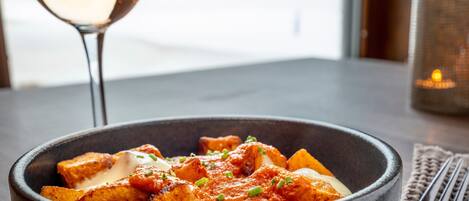A bowl of food on a table with a glass of white wine and a candle in the background.