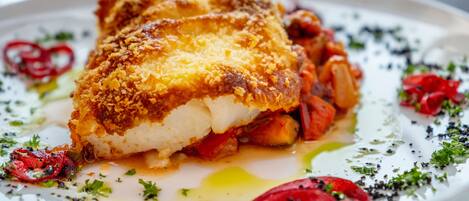 A plate with a breaded fish fillet, vegetables, and garnishes.