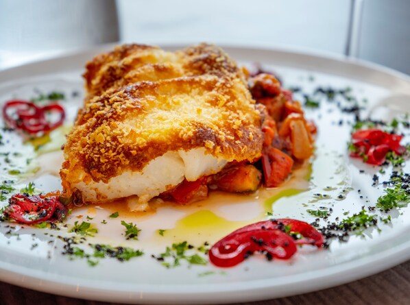 Un plato con un filete de pescado empanizado, verduras y guarniciones.
