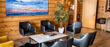 A wooden interior with a table and chairs, a painting, a plant, and a sign indicating room numbers.