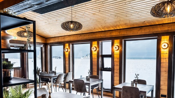 A restaurant with wooden walls and large windows overlooking a body of water. Tables and chairs are arranged for dining. - Lighthouse Inn (Suðurnesjabær)