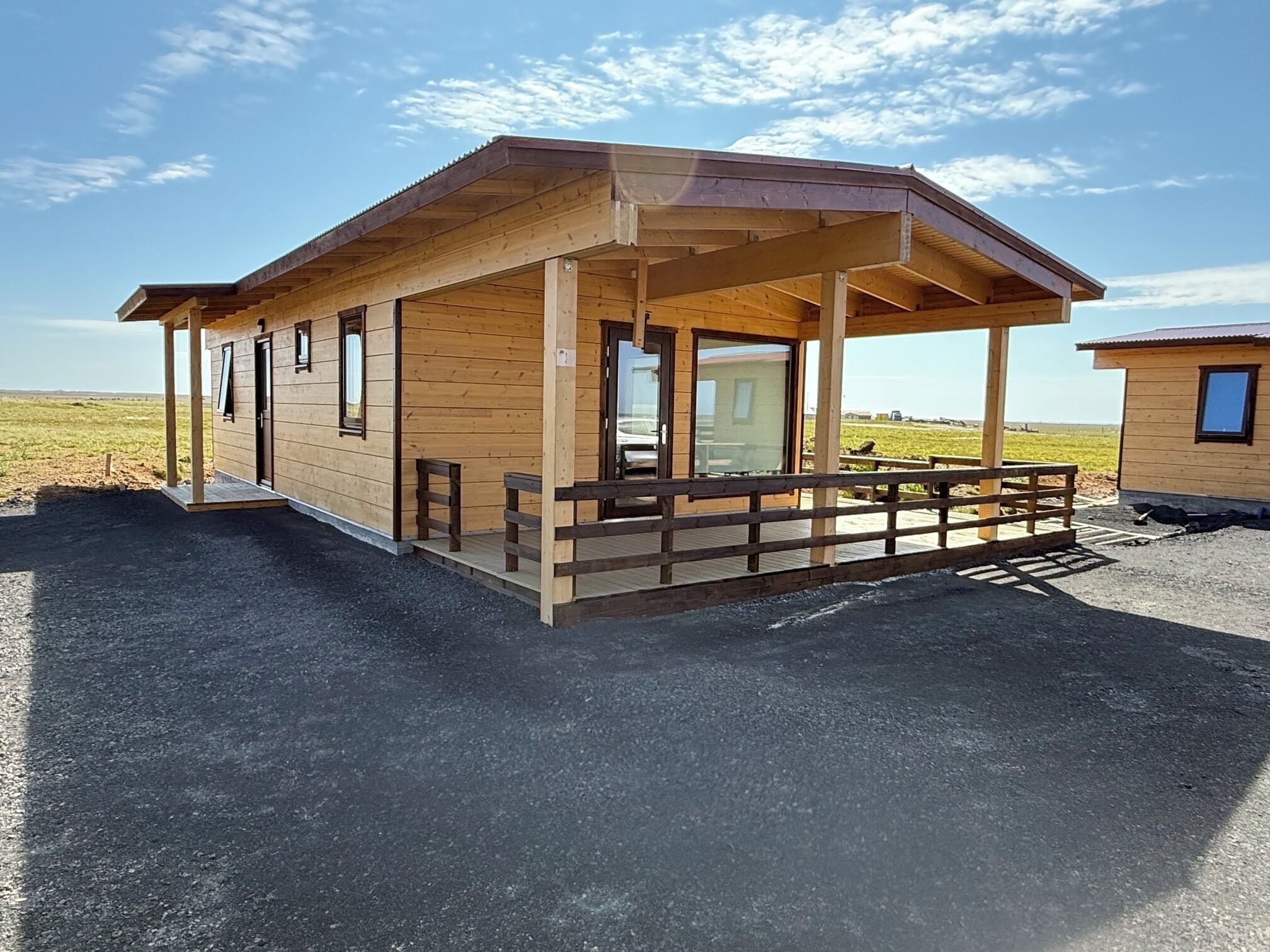 Une cabane en bois dotée d’un porche, de grandes fenêtres et d’une terrasse délimitée par une clôture.