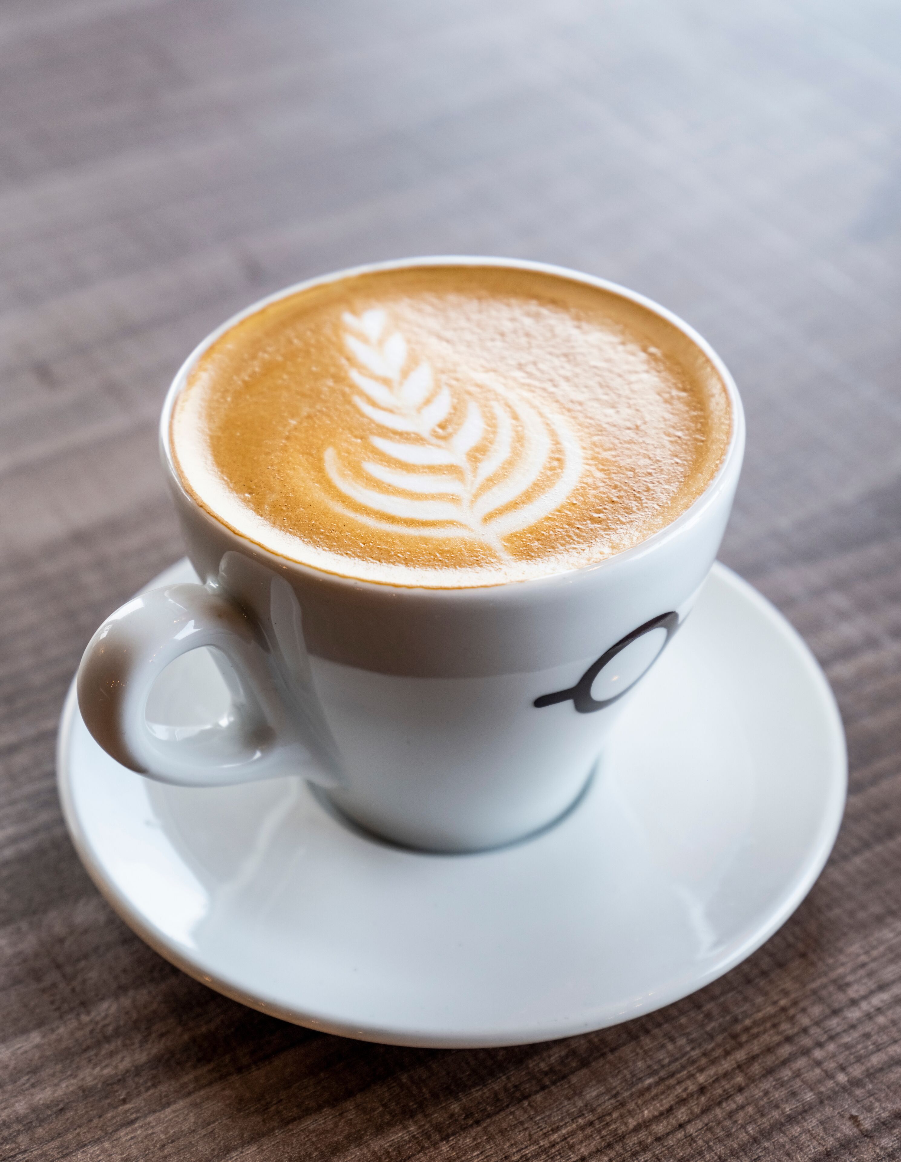 A white cup with a latte art design on a saucer.