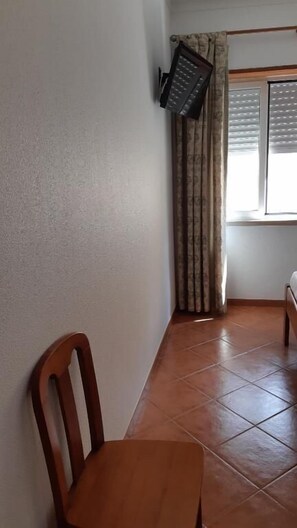 A room with a wooden chair, a tiled floor, a window with blinds, and a curtain. - Alojamentos S.José (Peniche)