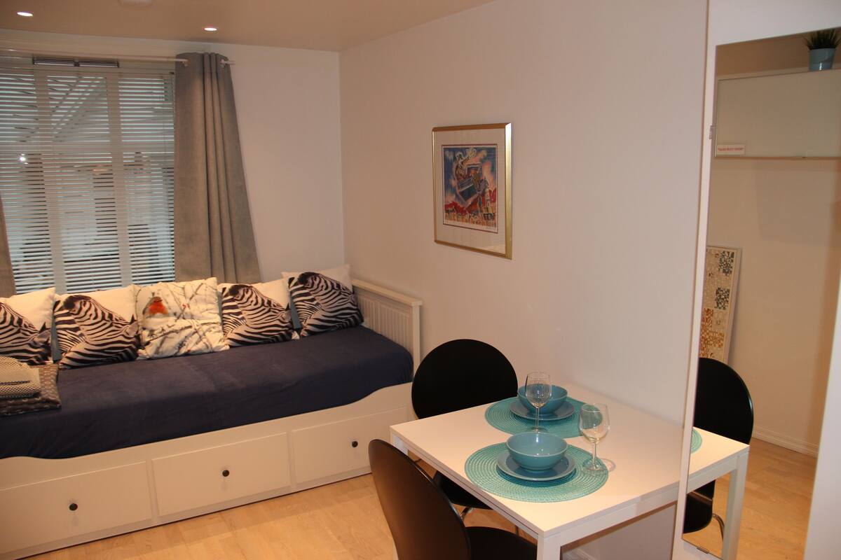 A bedroom with a bed, a dining table with chairs, and a window with blinds.