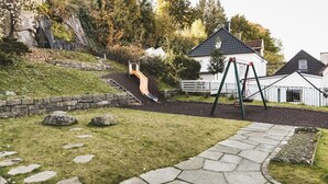 A playground with a slide and swings, surrounded by a stone wall and grass. - Skuteviken Apartments (Bergen)