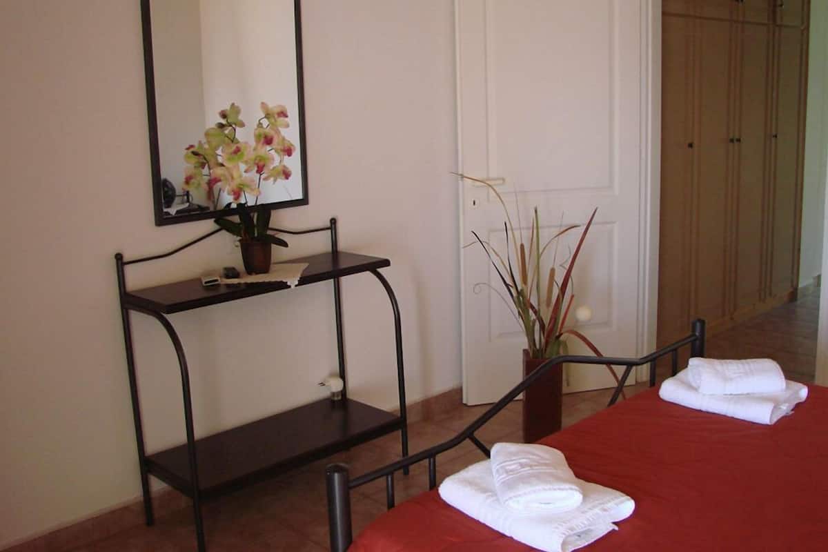 A hotel room with a bed, a bedside table with a mirror, a potted plant, and a door leading to a wardrobe.