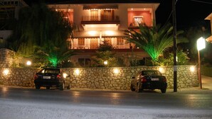 A two-story building with a stone wall and two cars parked in front. - Christianna Studios (Lefkada)
