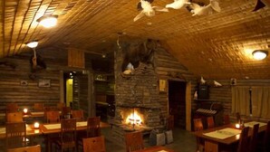 A rustic interior with wooden walls, a stone fireplace, and tables with candles. - Immelkartano (Kittila)