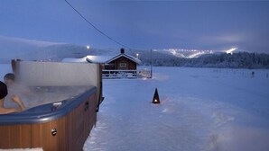 A wooden hot tub in a snowy landscape with a cabin in the background. - Immelkartano (Kittila)