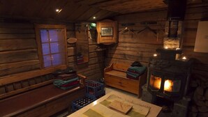 A cozy cabin interior with a wooden bench, a small table with a mat, a fireplace, and a window with a view. - Immelkartano (Kittila)