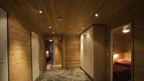 A wooden interior with a stone-patterned floor, wooden walls, and a hallway leading to a room with a bed. - Immelkartano (Kittila)