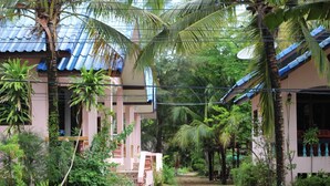 A pathway leading to a building with a traditional roof, surrounded by lush greenery and palm trees. - Chaiwat Resort (Laem Sing)