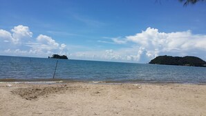 A sandy beach with calm water, a small island in the distance, and a clear sky. - Chaiwat Resort (Laem Sing)