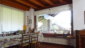 A dining area with a table set for four, wooden chairs, a radiator, and a view of a stone building outside. - La Rouine - Morgex (Morgex)