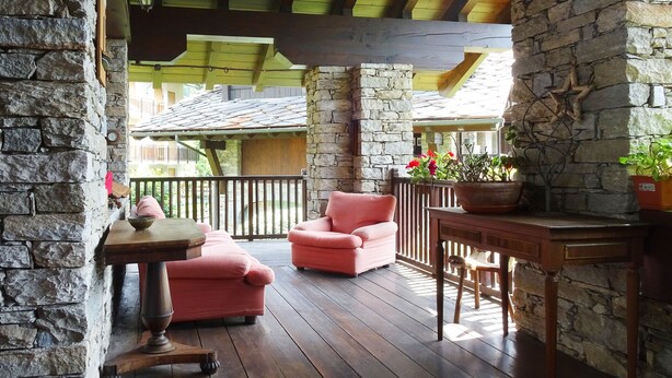 A wooden deck with stone walls, a table, two pink chairs, and potted plants. - La Rouine - Morgex (Morgex)