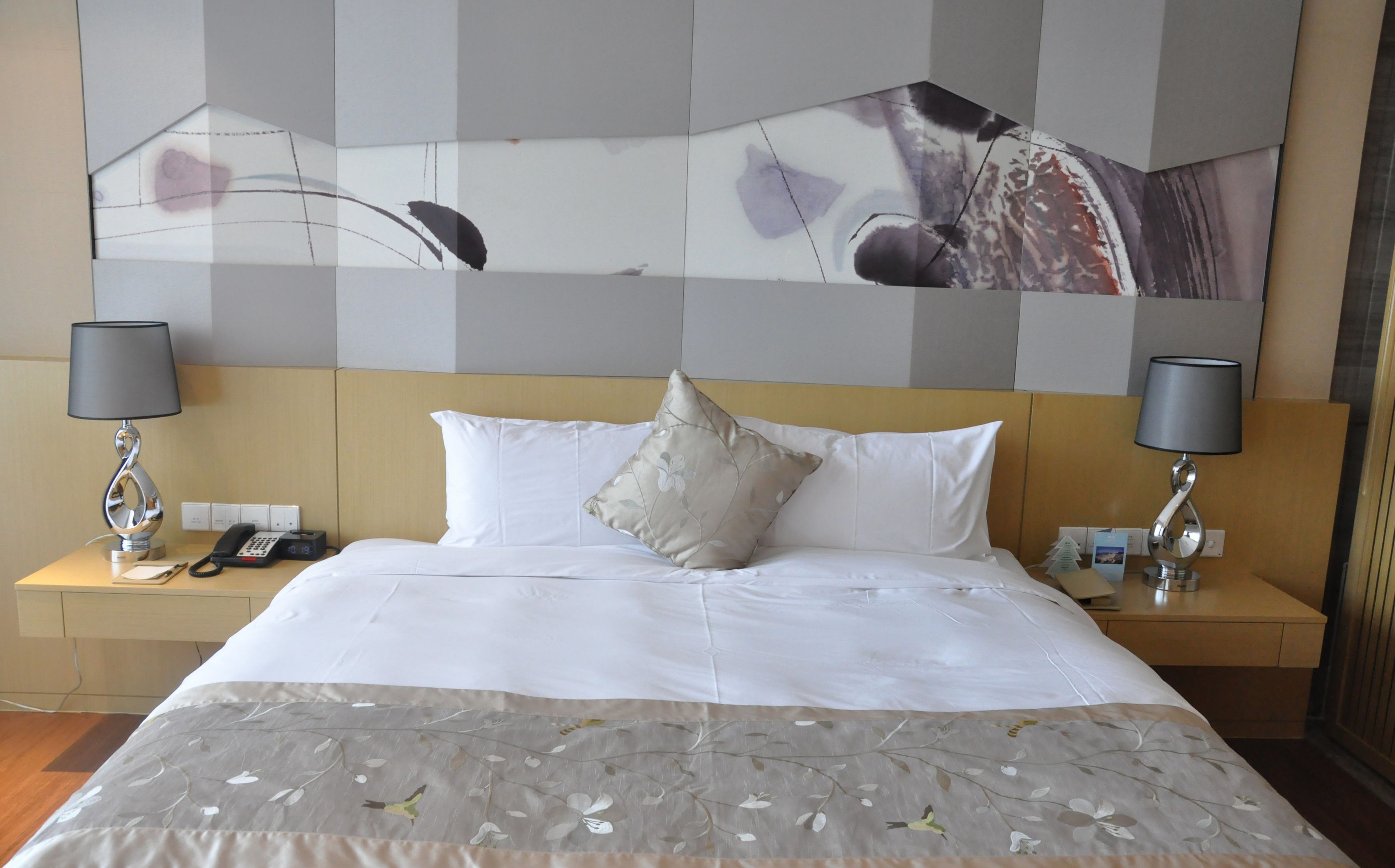 A hotel room with a large bed, two bedside tables, a telephone, and a wall-mounted artwork.