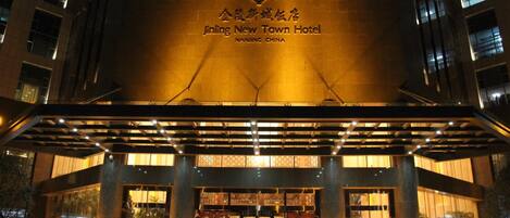 Exterior del Hotel Jinling New Town con señalización iluminada y un acceso cubierto.