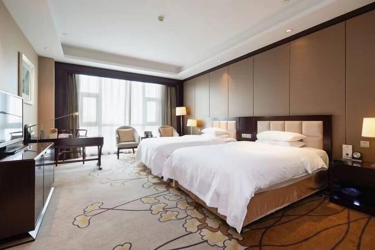A hotel room with two beds, a desk, and a TV.