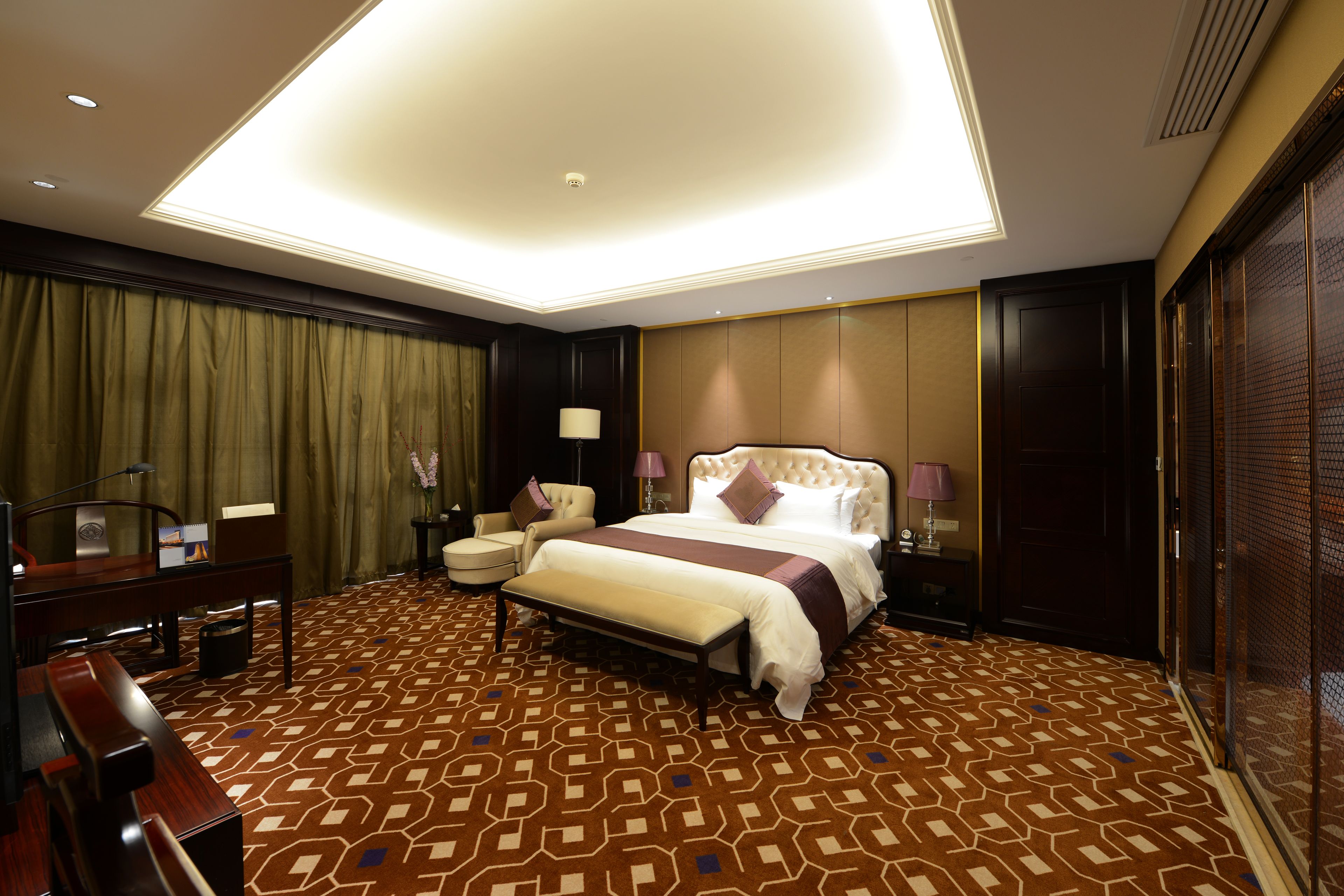 A hotel room with a large bed, a desk, a chair, and a bench.