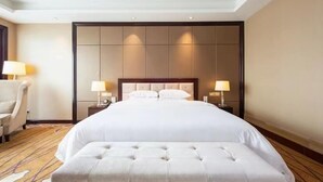 Habitación de hotel con una cama grande, dos mesitas de noche con lámparas, una silla y un banco.