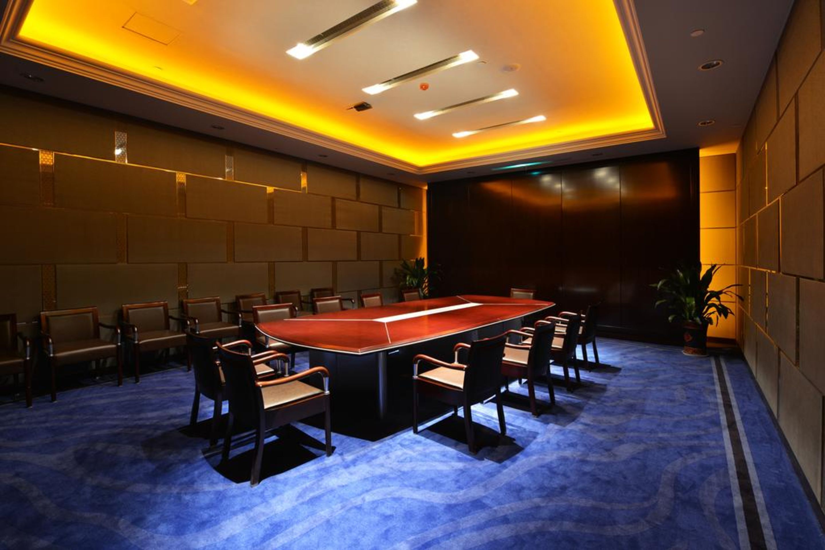 Un salón de conferencias con una mesa rectangular rodeada de sillas, alfombra azul e iluminación empotrada en el techo.