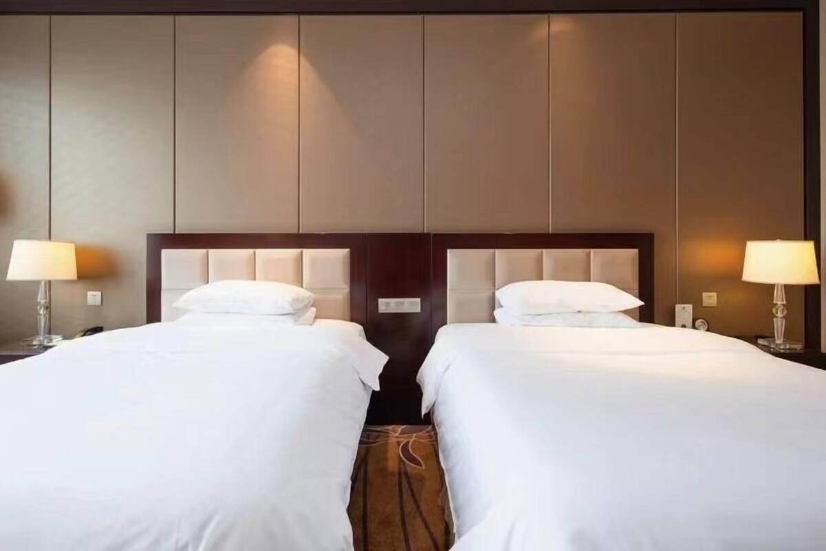 A hotel room with two beds, each with a headboard and bedside lamps.