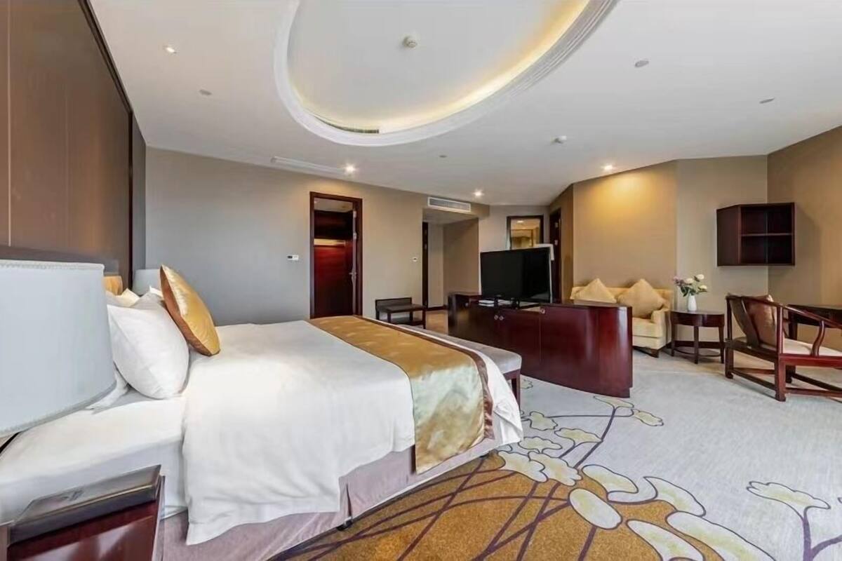 A hotel room with a large bed, a desk, a television, and a seating area.