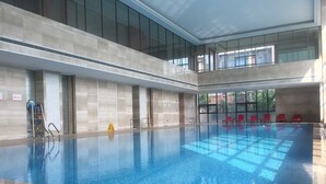 An indoor swimming pool with clear water, a tiled floor, and red chairs along the side. - Jinling Yew Resort Wuxi (Wuxi)
